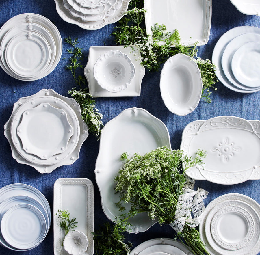 An array of white juliska dinnerware and serveware spread out over a blue table