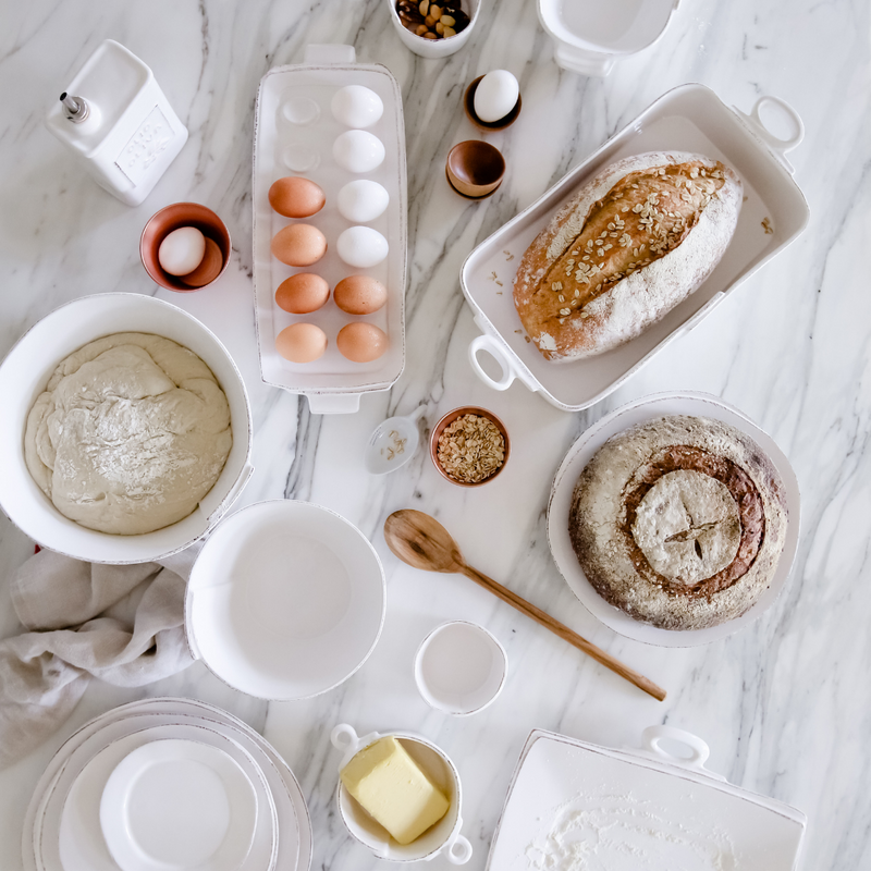 top down view of white Lastra bakeware. Some of the pieces are full of fresh baked bread, eggs, butter and other cooking supplies. 