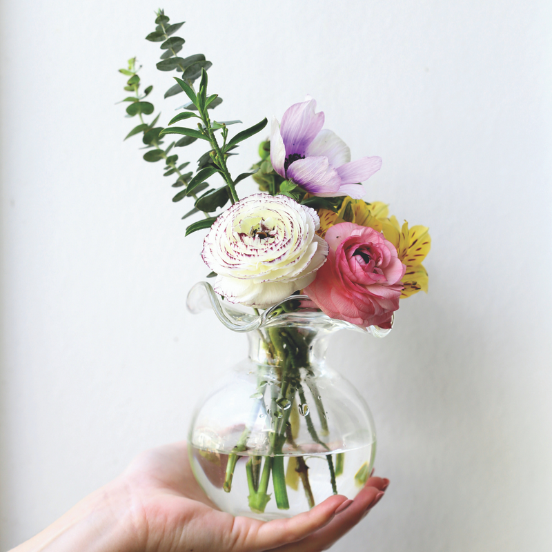 An outstretch hand holding a small clear bud vase that is full of fresh flowers. 